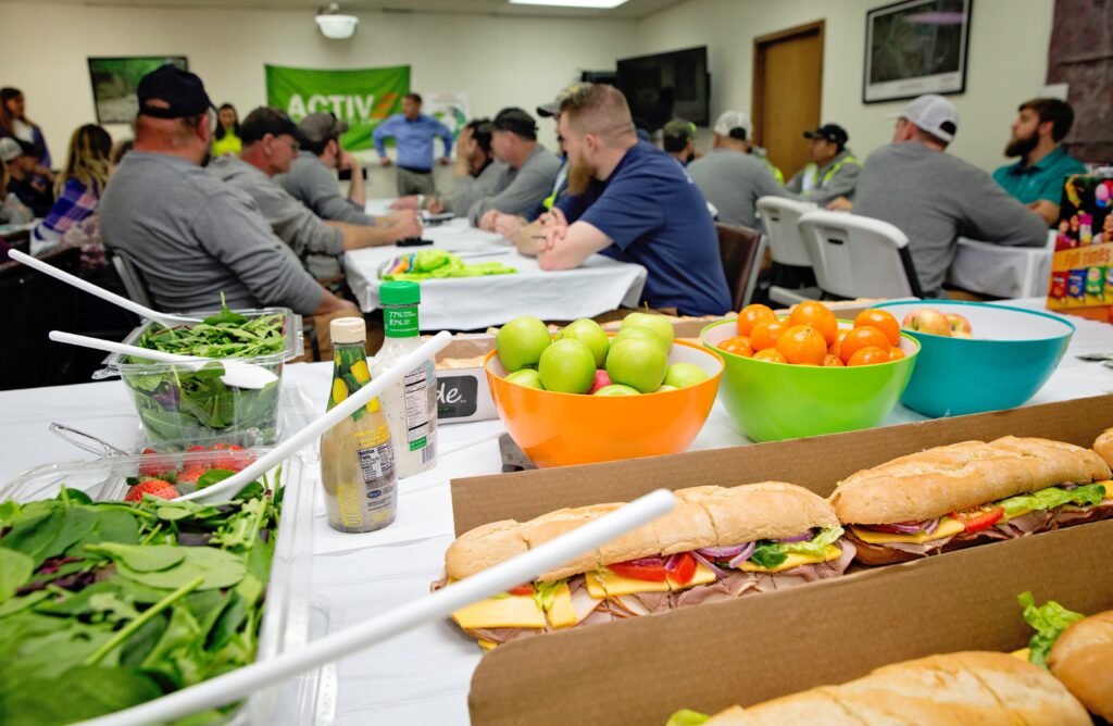 Healthy lunch in the foreground with a workplace lunch meeting proceeding in background.